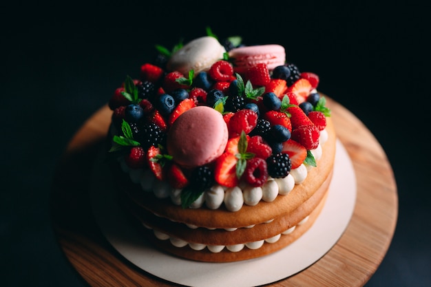 Cake decorated with berries on a wooden stand on black