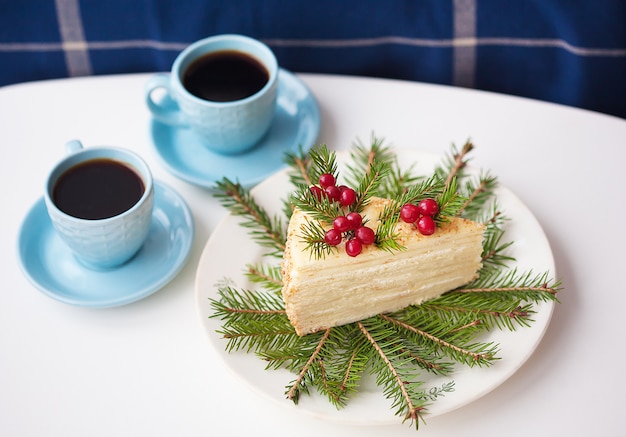 Cake decorated with tree branches and berries with two cups of coffee