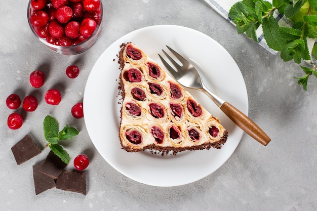 Cake met kersen, room en chocolade op een witte plaat op een lichte achtergrond