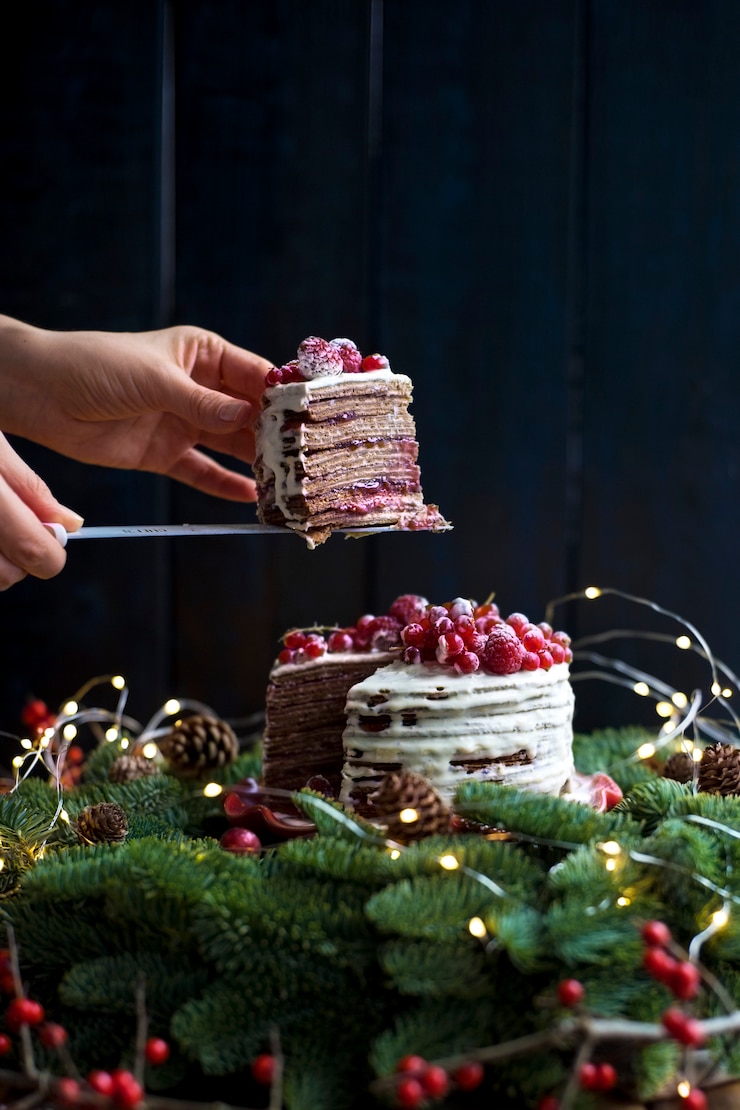 Foto cake met rode bessen in handen in de buurt van de kerstboom