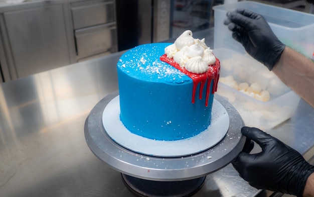 Cake pastry chef designer decoration a blue frosted icing cake for further decoration with red dripping with ganache and white meringues on top