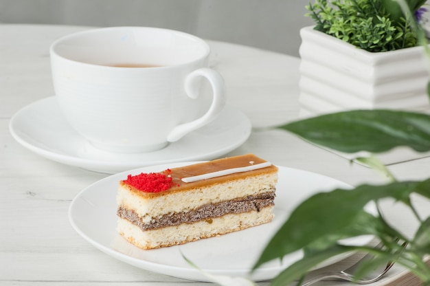 Cake on a plate and a cup of coffee on a table with flowers