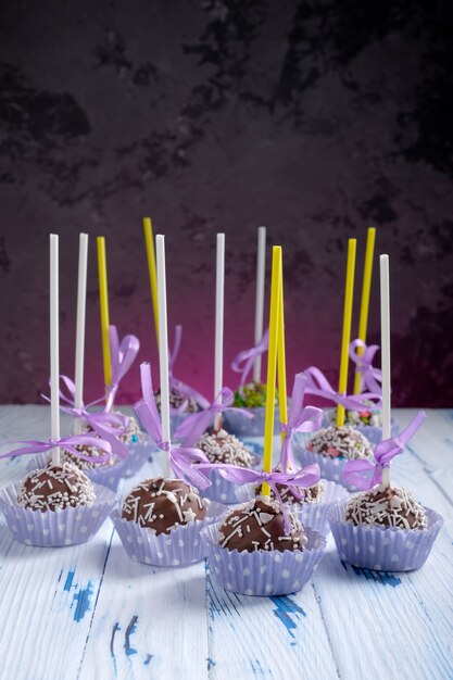 Cake pops coated chocolate with sprinkling on wooden table table on dark background with copy space