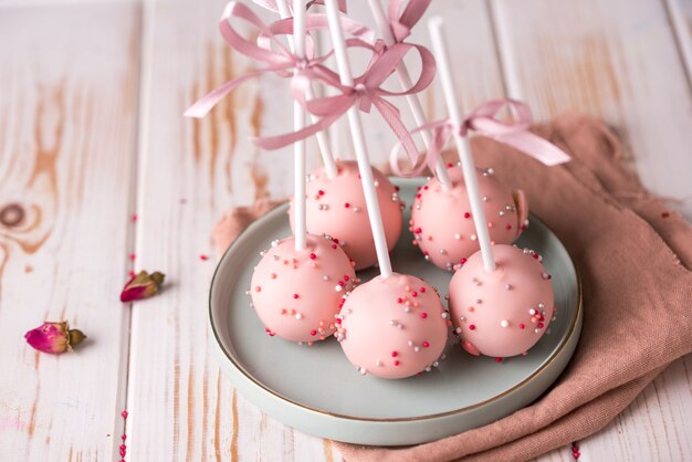 Cake pops in pink cream lie on a beautiful plate. Delicious close-up dessert.