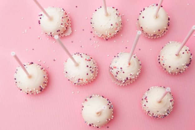 Cake pops on a stick in white glaze and colored powder on a pink surface. Tasty and beautiful sweets for birthday or party