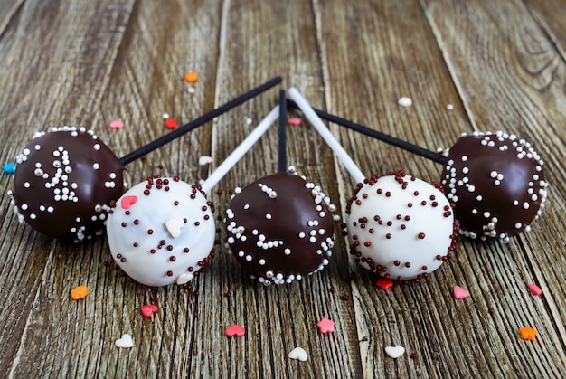 Cake pops. Sweet sweets in white and black chocolate glaze, on a stick on a wooden background. Food background.