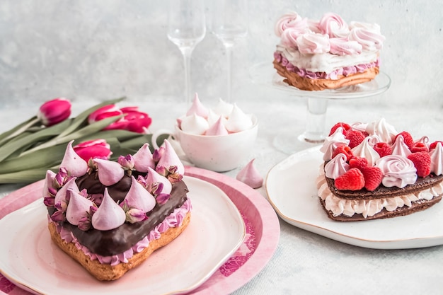 Cake in the shape of a heart from Traditional French dessert eclair and Pavlov cookies on a white background with tulips and glass glasses Valentine's day concept