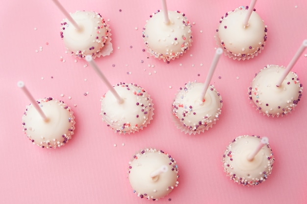 Cake springt op een stok in wit glazuur en gekleurd poeder op een roze oppervlak. Lekkere en mooie snoepjes voor verjaardag of feest