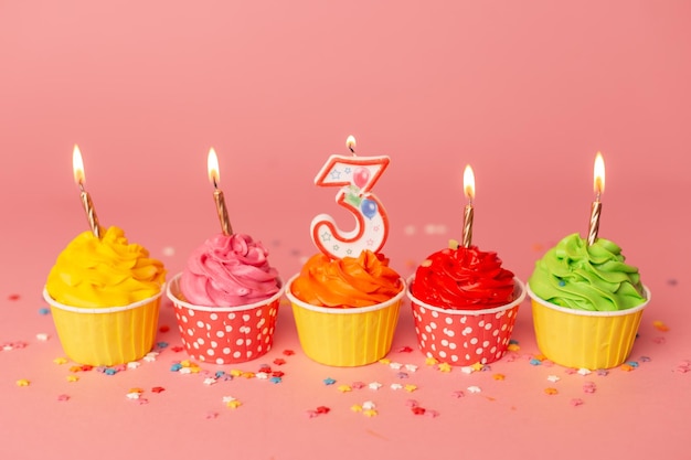 3歳の誕生日のケーキピンクの背景にカラフルなケーキの中でカップケーキのキャンドル番号3