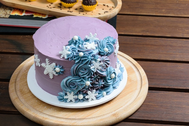 Foto torta con crema al burro decorata con fiocchi di neve e perle sul tavolo di legno.