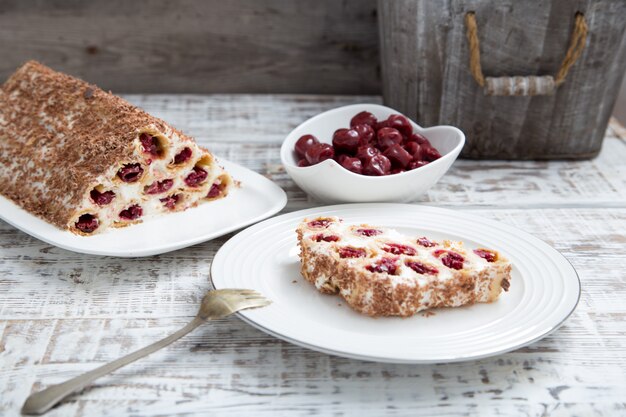Cake with cherries, cream and chocolate on a light wooden background