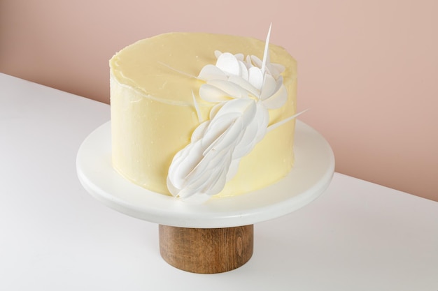Cake with cream decorated with Wafer Paper sheets on white wooden cake stand on beige background