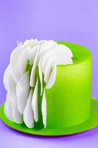 Photo cake with green cream icing and white leaf decorations on purple background close up