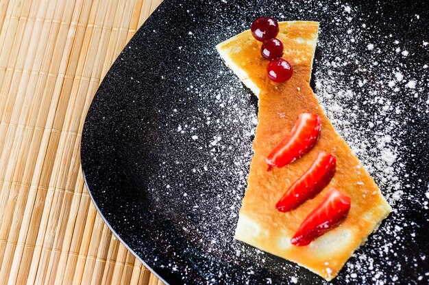 Photo cake with pieces of strawberry and cherries on black plate with poudre