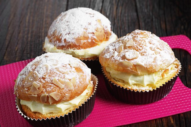 Cake with whipped cream and almonds on red kitchen board on table