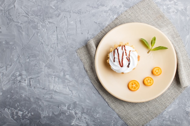 Cake with whipped egg cream on a light brown plate with kumquat and mint leaves