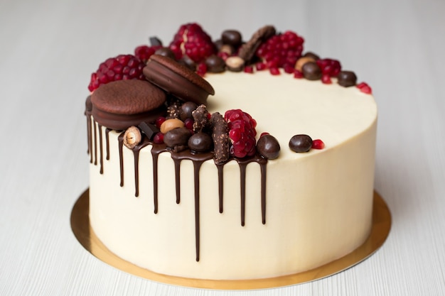 Photo cake with white cream, chocolate drips, pomegranate, nuts and chocolate decor