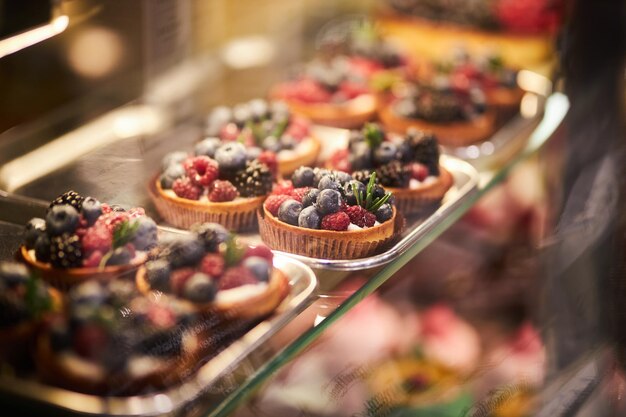 Cakes on a glass counter in a bakery cakes with fresh berries\
tartlets with yogurt raspberries