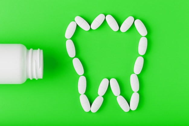 Calcium vitamin in the form of a tooth spilled out of a white jar on a Green .