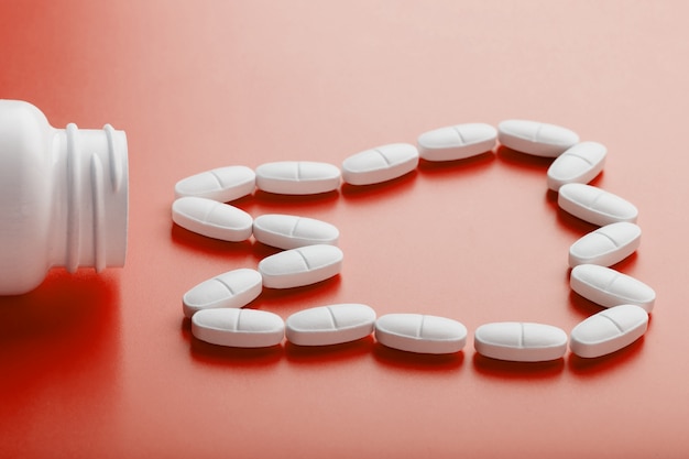 Photo calcium vitamin in the form of a tooth spilled out of a white jar on a red .