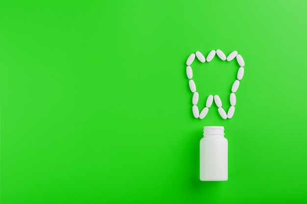 Calciumvitamine in de vorm van een tand die uit een witte pot op een Green is gemorst.