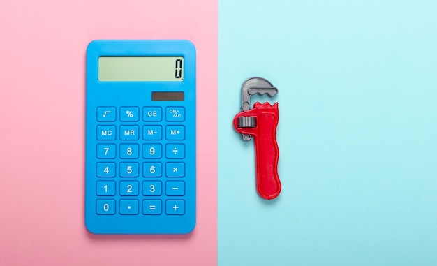 Расчет стоимости ремонтных работ. Калькулятор и игрушечный ключ на сине-розовом пастельном фоне. Вид сверху