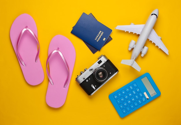 Calculation of the cost of tourism or resort. Flat lay. Figurine of passenger plane, calculator, flip flops, passport, camera on yellow