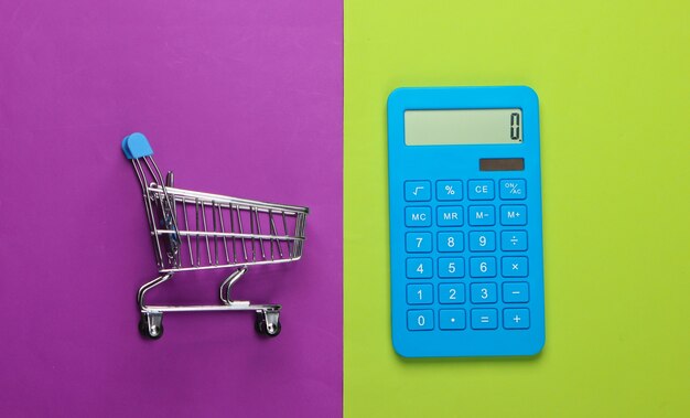 Calculation of costs for shopping, purchases in the supermarket. Calculator and shopping trolley on green-purple background. Top view. Minimalism