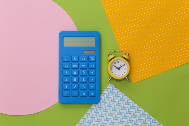 Calculator and alarm clock on creative colorful paper background.