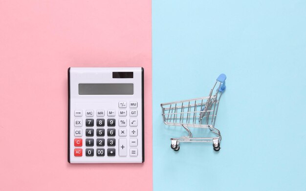 Фото Калькулятор и тележка для покупок на сине-розовом пастельном фоне вид сверху