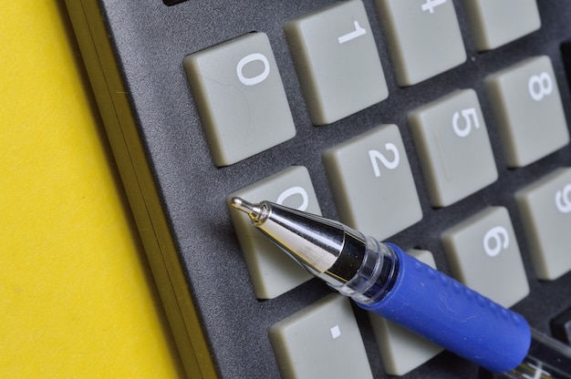 calculator and ballpoint pen lie on a yellow background. close-up.