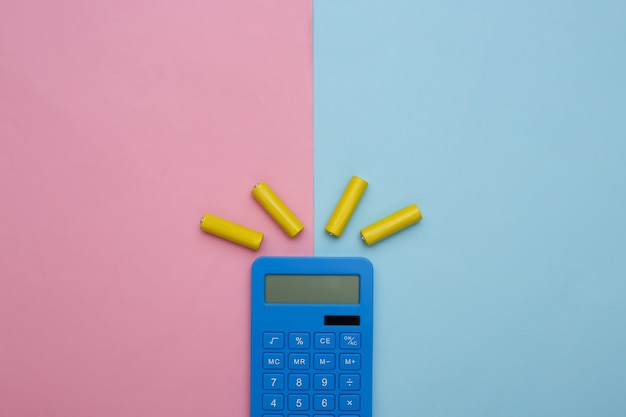 青ピンクのパステルカラーの背景に電卓と電池。上面図