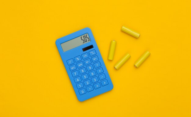 Calculator and batteries on yellow background. Top view