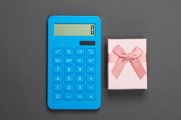 Calculator and gift box with bow on gray. Calculation of the value of the gift.