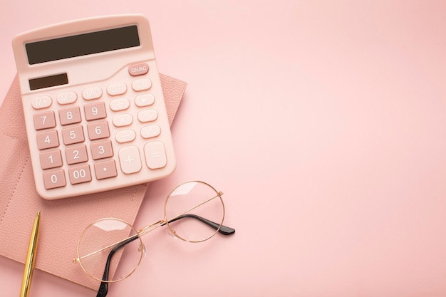 Calculator glasses and notepad on a pink background Place for text