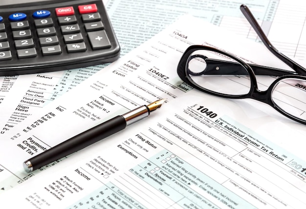 Calculator, glasses and pen on tax form 1040.