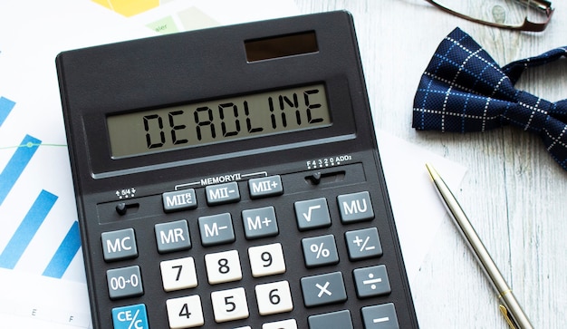 Калькулятор с надписью DEADLINE лежит на финансовых документах в офисе.