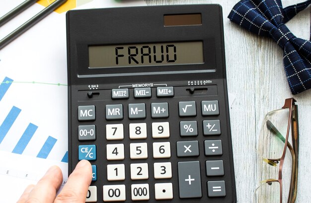 A calculator labeled FRAUD lies on financial documents in the office.