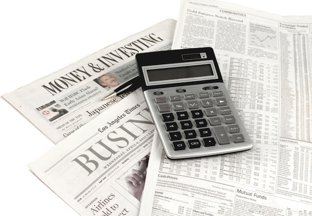 Calculator laying on newspapers with pen isolated on white