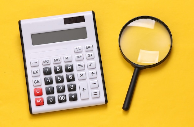 Calculator and magnifier on yellow background Top view