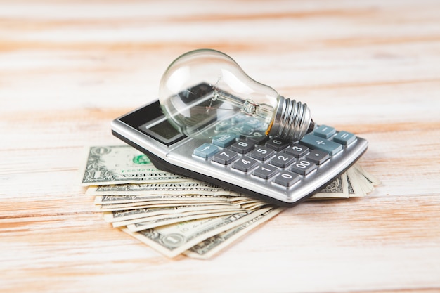 Calculator, money and light bulb on wooden scene