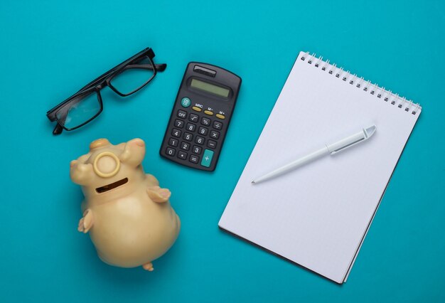 Calculator, notebook, glasses, piggy pank on blue.