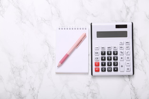 Calculator and notebook on marble surface Top view