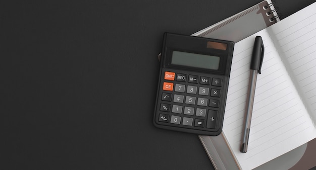 Calculator, notebook, pen on black leather background. Top view with copy space. Flat lay composition.