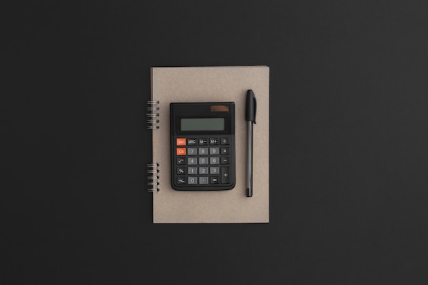 Calculator notebook pen on black leather background