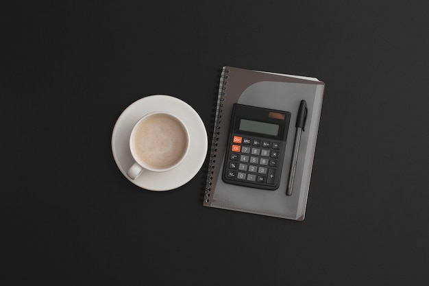 Penna per taccuino calcolatrice e una tazza di caffè su fondo in pelle nera