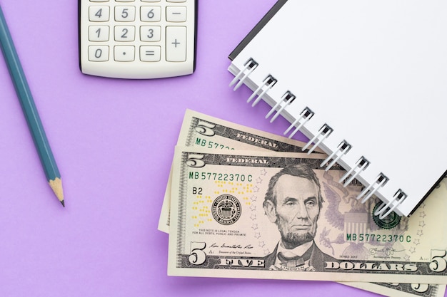 Calculator, notebook with american money and a pencil on a lilac table