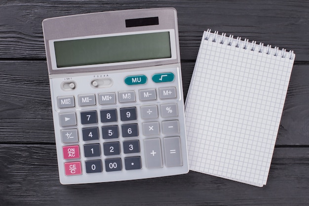 Calculator and notepad on dark wooden table. Top view flat lay.