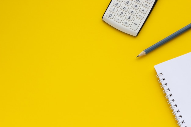 Калькулятор, блокнот и карандаш на желтом фоне, место для текста