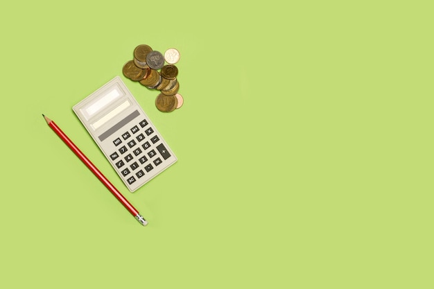 A calculator a pencil and a heap of coins on a green background with copy space